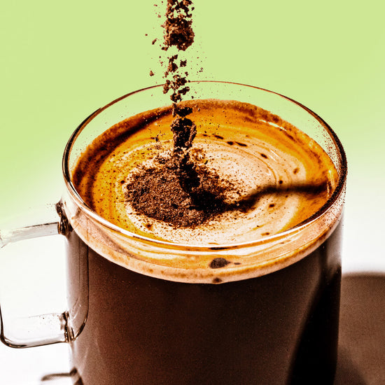 powdered coffee falling into a frothy clear mug of coffee