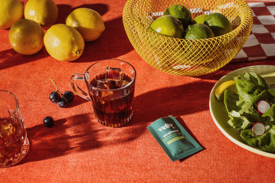 iced coffee on table surrounded by fruits, vegetables, and Velty packet 